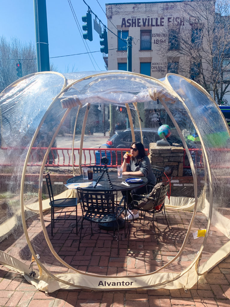 a woman sips her drink inside of a covid dining bubble outside of a restaurant in downtown Asheville