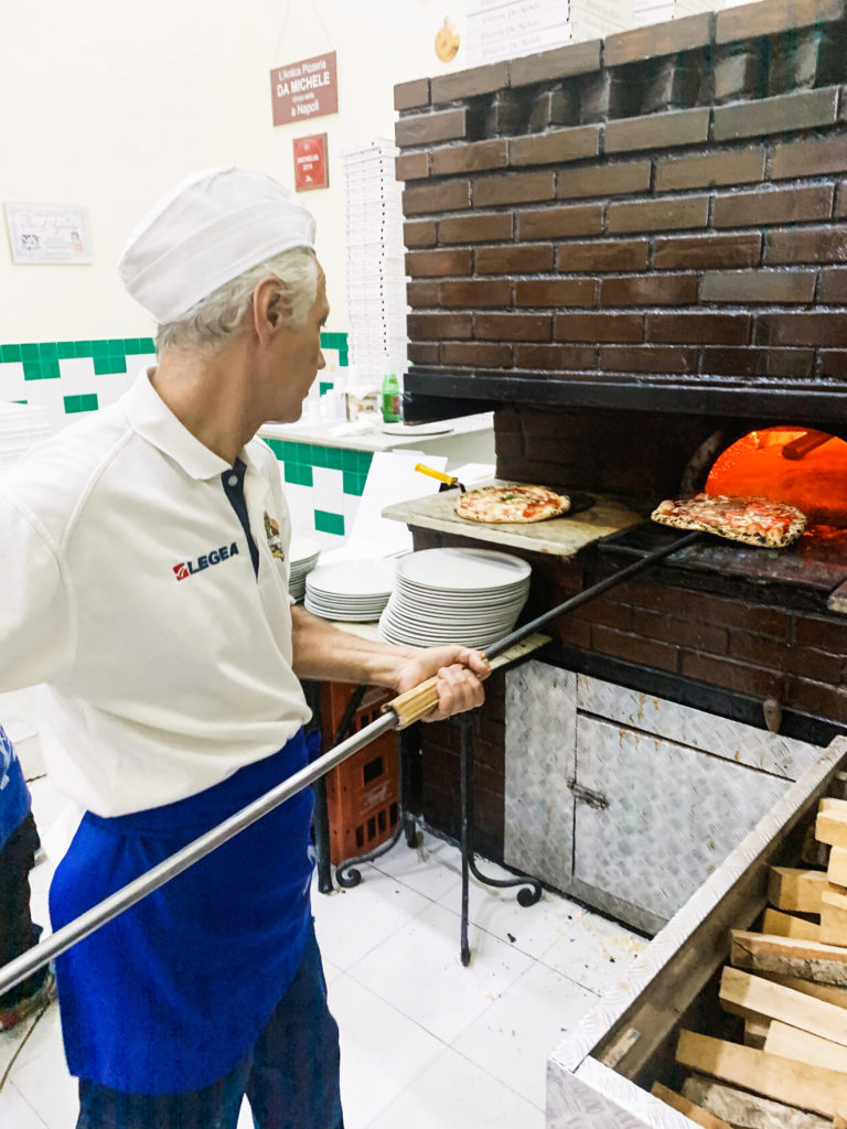 a chef putting pizza into the pizza oven at L'Antica Pizzeria da Michele