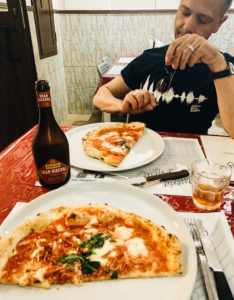 a man eating half of a Neapolitan pizza with a beer in Naples, Italy
