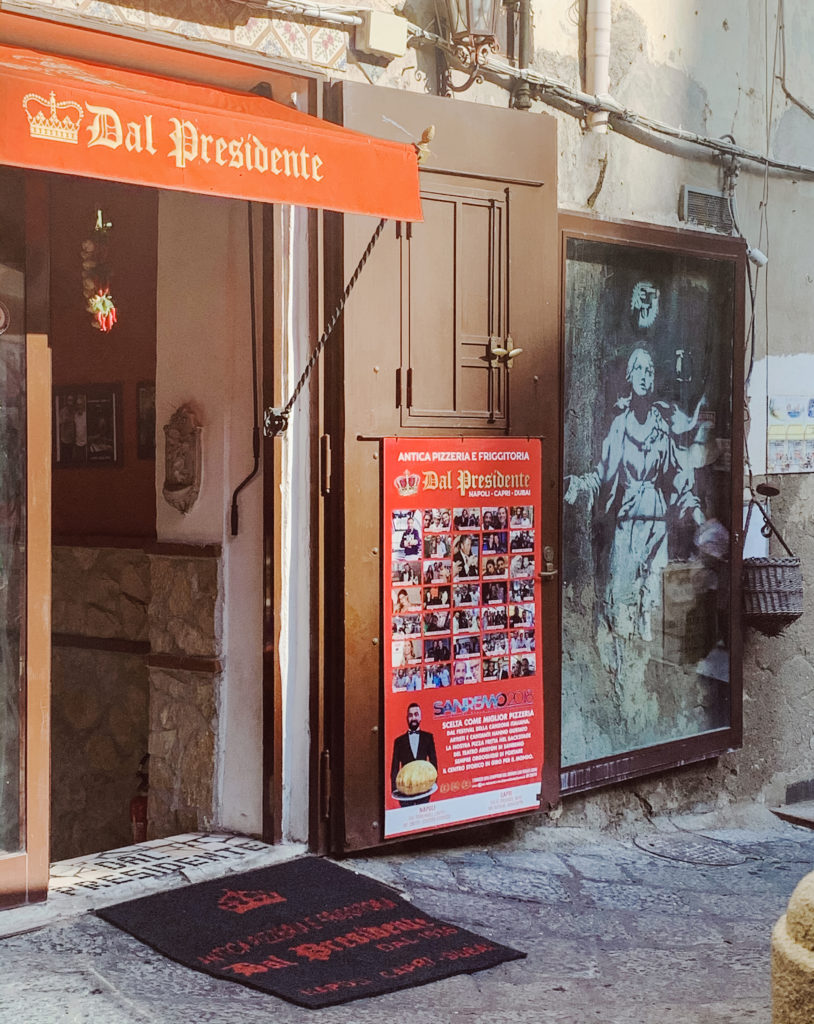 exterior of Pizzeria Dal Presidente in Naples, Italy with a Banksy artwork next to the door