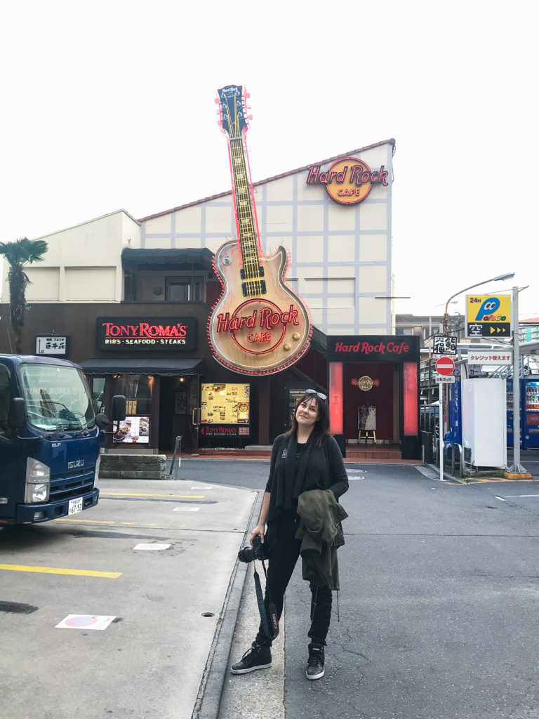 a woman stands posing in front of the Hard Rock Cafe in Tokyo