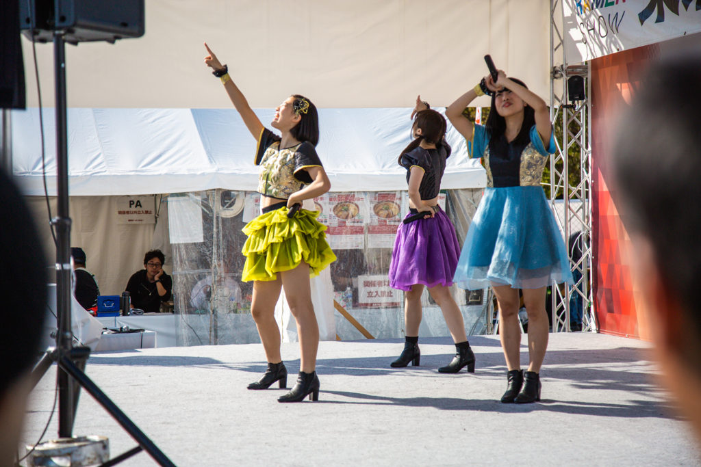 a trio of female J-Pop performers on an outdoor stage