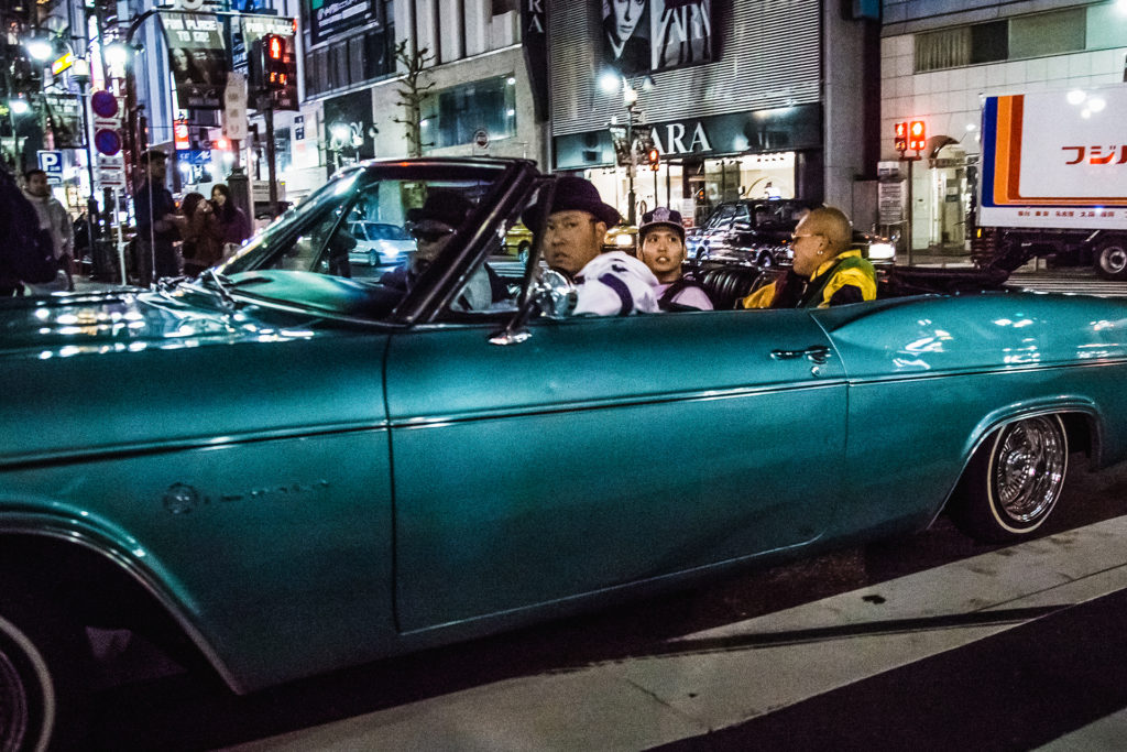 a teal low rider car cruises on a Friday night in Shibuya