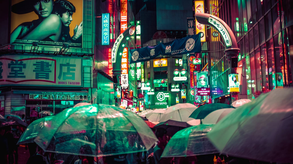 neon signs and the tops of a crowd of umbrellas on a rainy night in a city in Japan