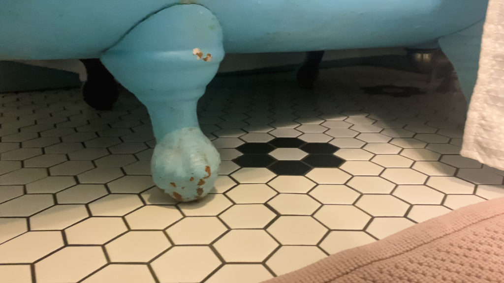 the foot of a blue clawfoot bathtub on a vintage tile floor