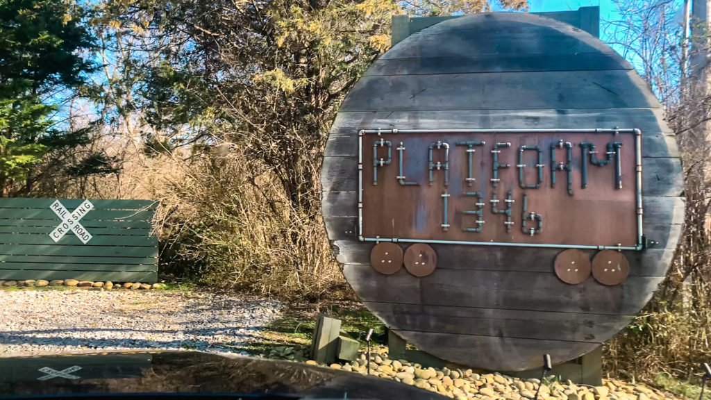 a railroad crossing sign and large wooden sign designating the entrance to Platform 1346, the location of a WWII-era train car that can be rented on airbnb