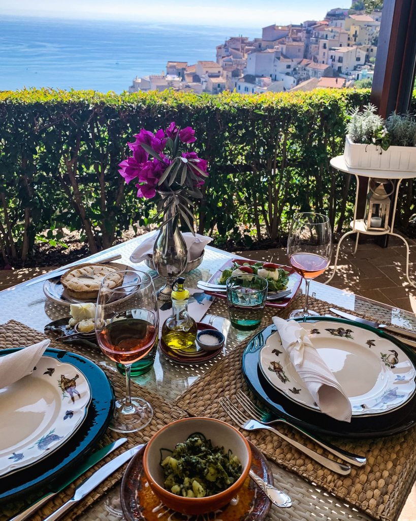 the view of the Amalfi Coast from a terrace with a table set for a multi-course lunch with wine. taken at an organic winery on the amalfi coast.