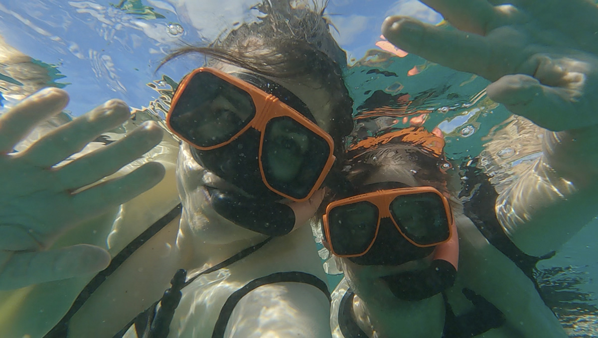 woman and man wearing snorkeling masks and snorkels, underwater side by side waving at the camera during a snorkeling excursion in the U.S. Virgin Islands.
