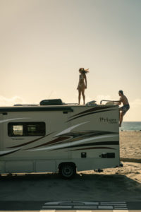man and woman climbing onto roof of an RV at sunset