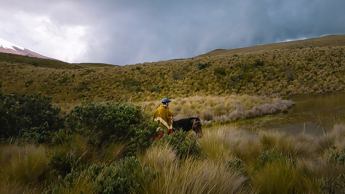 man wearing a poncho and helmet riding horseback at Cotopaxi National Park in Ecuador, South America