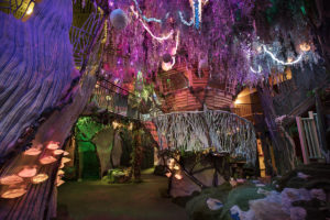 dark interior view of one of the locations in Meow Wolf's House of Eternal Return, Santa Fe, New Mexico with colorful lights and an indoor tree