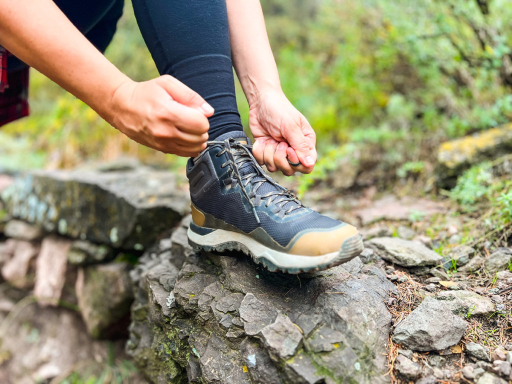 A photo of a woman's foot on a large rock as she ties her grey and tan North Face hiking shoe.