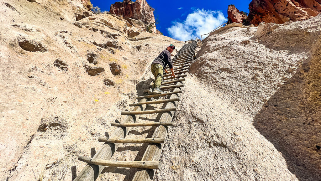 man climbing very tall handmade ladder of the cliff dwellings at Bandelier National Monument in New Mexico