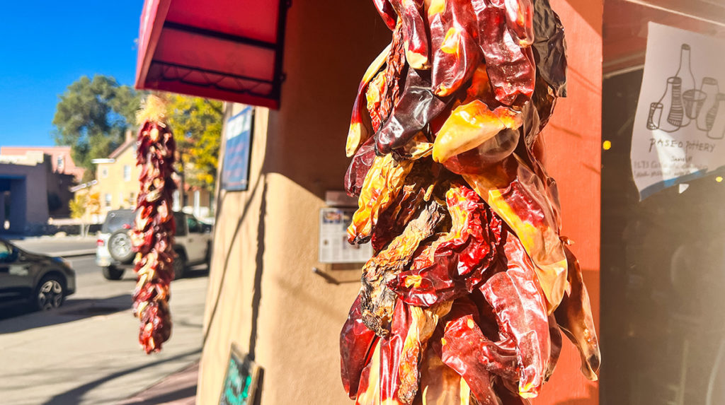 bunches of chilis hanging from an adobe building in the sun in Santa Fe, New Mexico