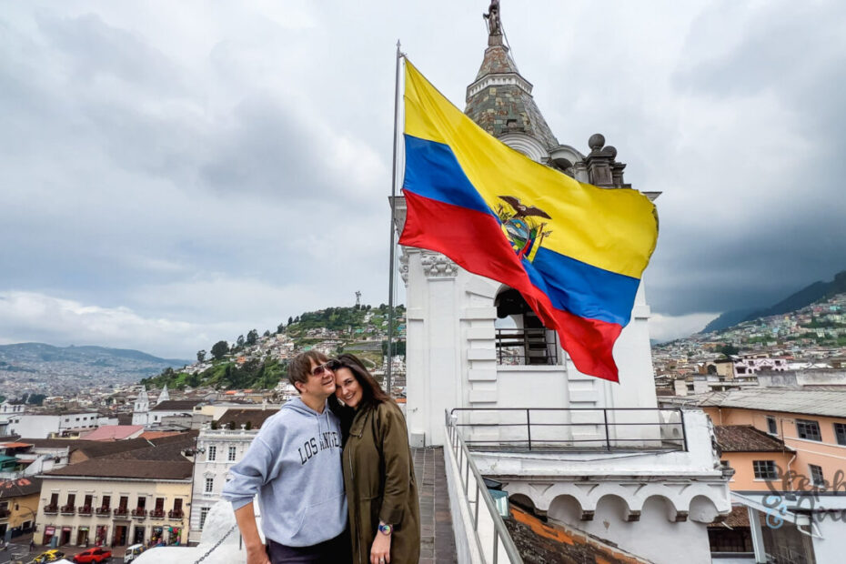 a man and woman pose on a rooftop in Quito with a large Ecuador flag behind them