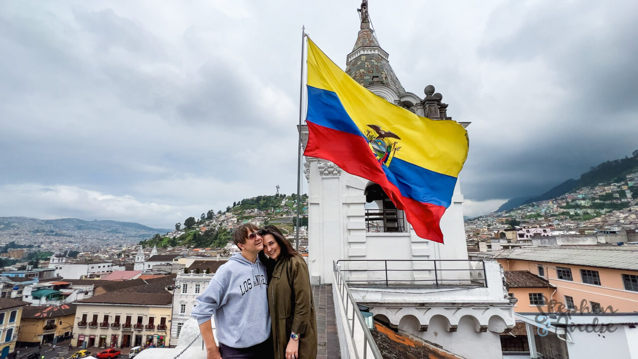 a man and woman pose on a rooftop in Quito with a large Ecuador flag behind them