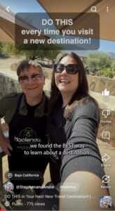 A man and woman taking a selfie in cooking aprons with the words saying "Do this every time you visit a new destination!"