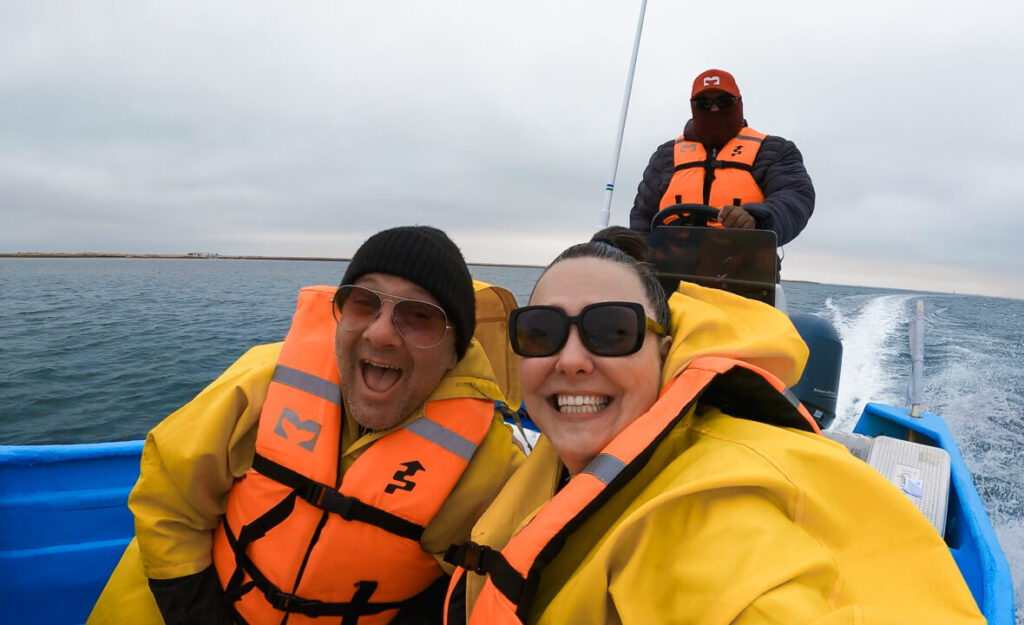 A man and woman take a happy selfie on a small boat in open water. 